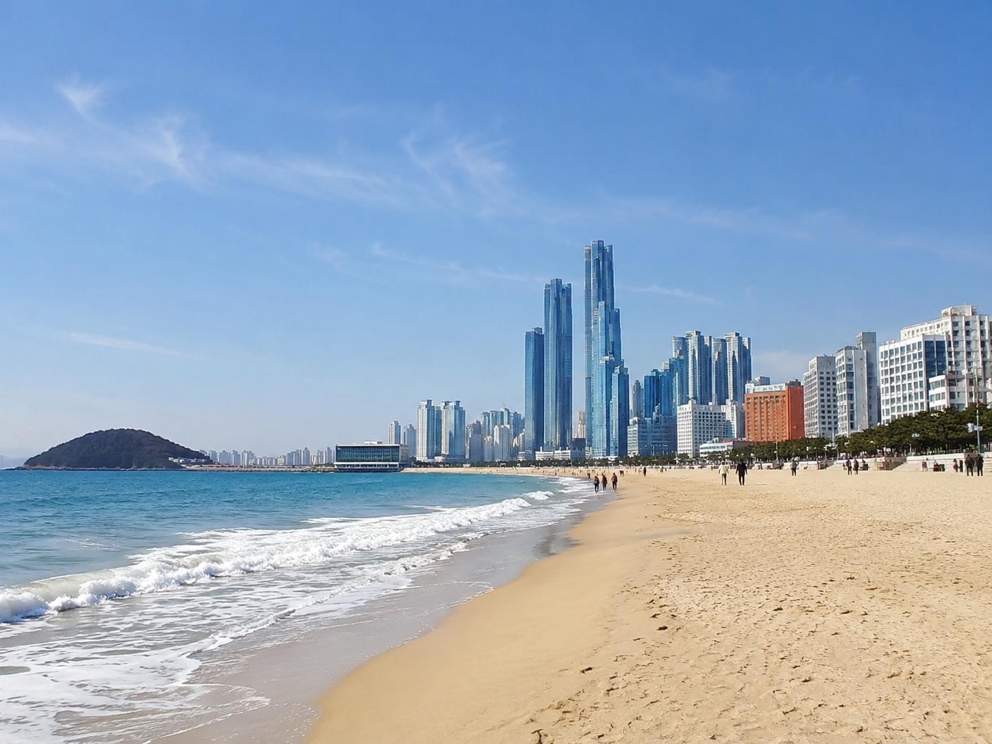 A bright, refreshing travel image showing Haeundae Beach together with the Busan city skyline