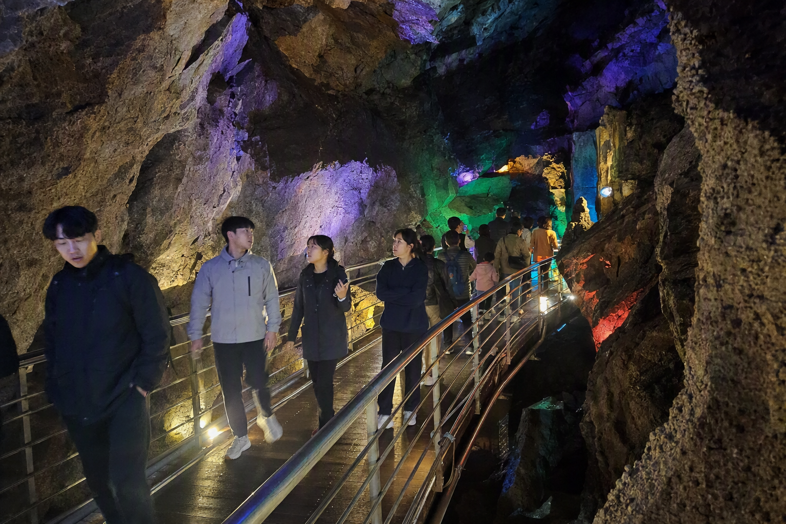 明亮鮮豔、寫實感十足的洞窟步道內部景象,燈光戲劇性照明,遊客行走其中,彩色光線映照在巖壁上,氛圍清涼