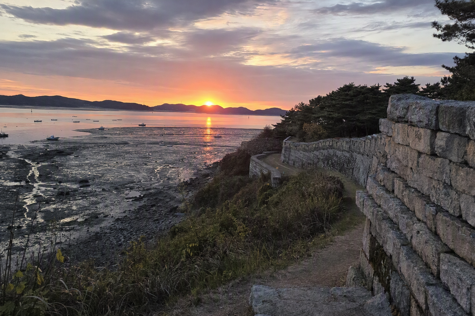 江華島海岸的明亮鮮豔寫實夕陽景色，有潮間帶、古老石砌城牆、平靜海面、溫暖橘色天空，畫面中無可見文字