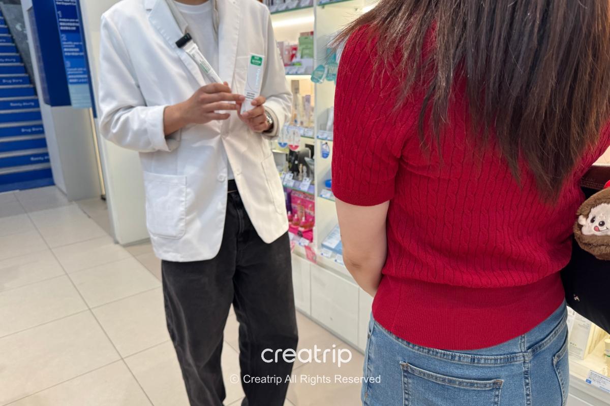 A staff member in a white coat inside a pharmacy talking with a member of the editorial team about a product