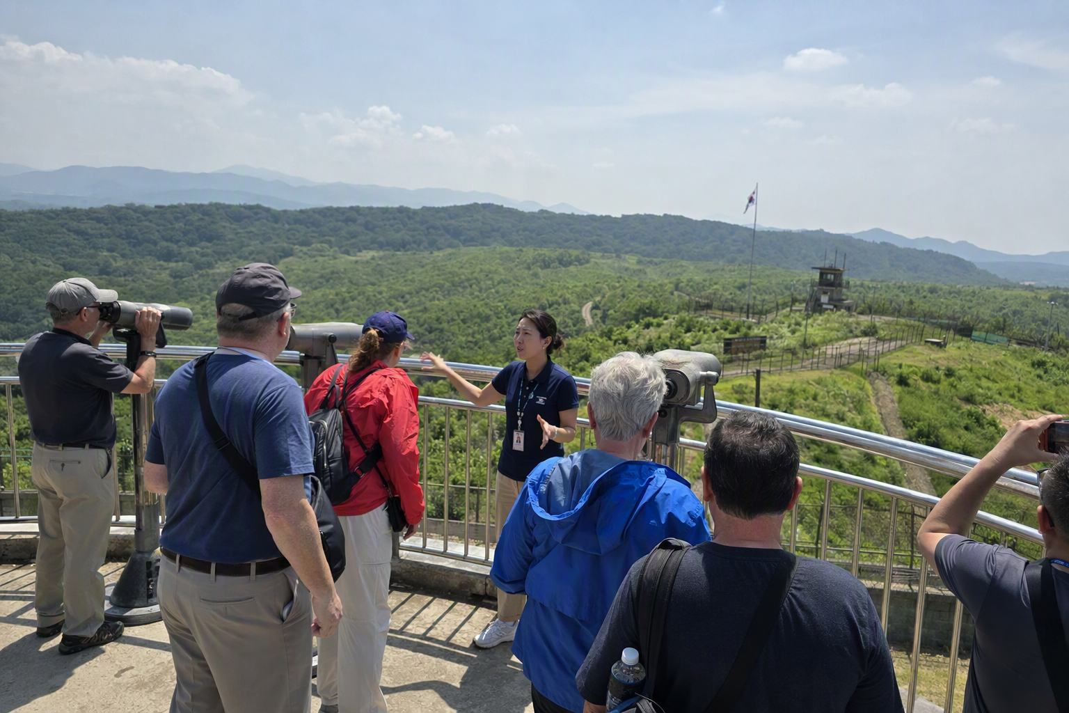 明亮、色彩鮮明、寫實風格的 DMZ 一日遊場景, 有導覽帶領的旅客在觀景區, 綠色丘陵與晴朗天空, 無可見文字