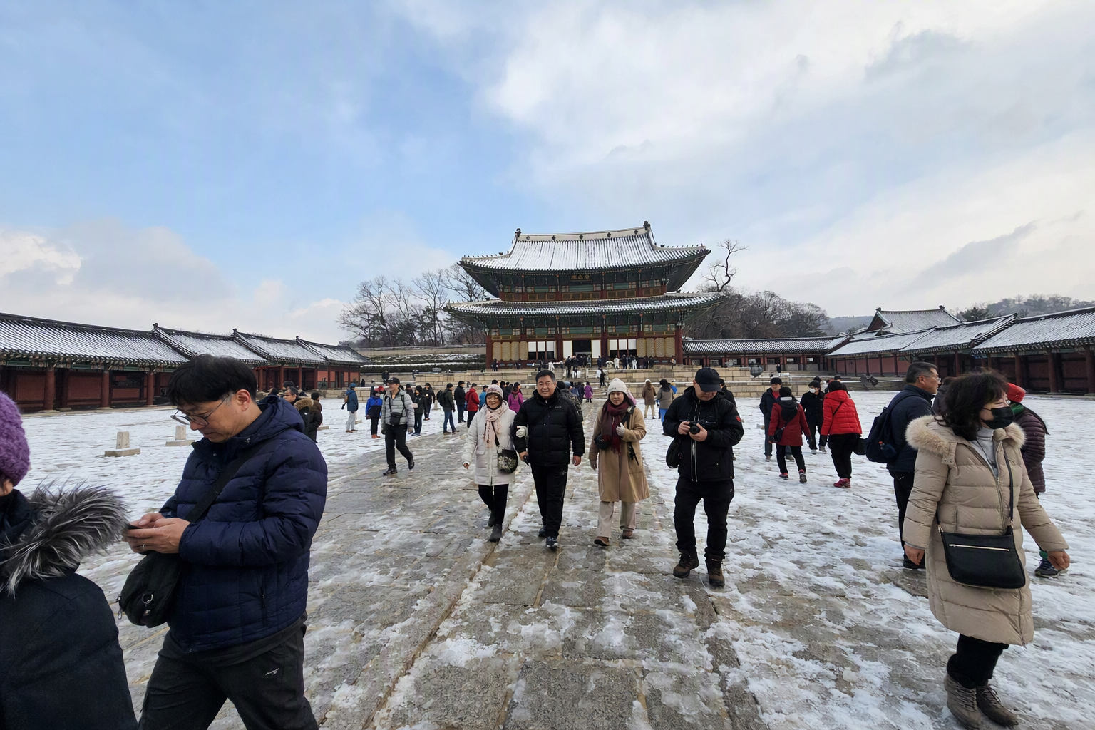 Bright vibrant photorealistic snowy morning at a Seoul palace courtyard, light snow on rooftops, bundled travelers, soft blue winter sky, no visible text