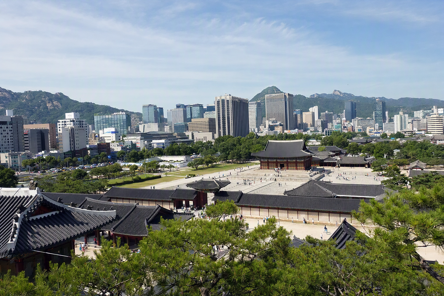 首爾明亮寫實景色，前景係傳統宮殿屋頂，後方係現代摩天大樓，藍天清澈，氣氛熱鬧但優雅，充滿旅行感