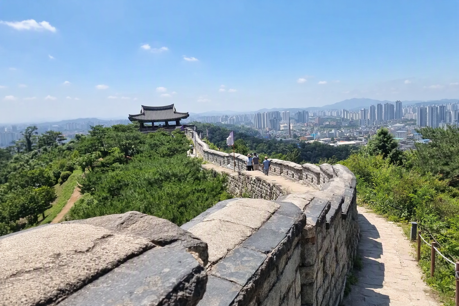 Bright, vibrant, photorealistic view of Suwon Hwaseong Fortress walls curving over a hill with gates, city skyline, blue sky, and soft sunlight, no Korean text