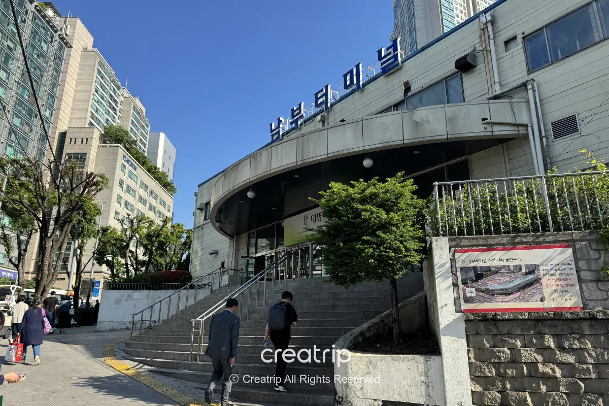 首爾南部客運站外觀入口與階梯,藍天下旅客提著行李準備進站,適合說明南部轉運站用途與搭車注意事項。