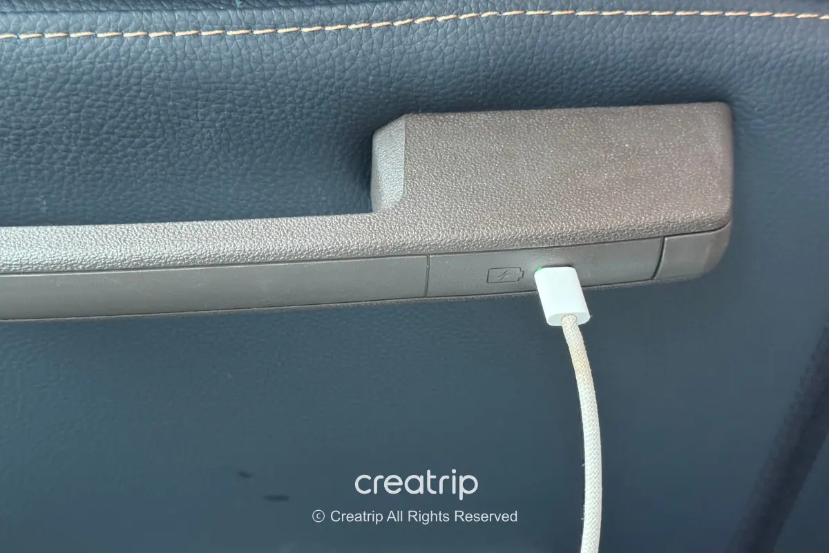 長途巴士座椅扶手下方的Type‑C充電孔插著充電線,顯示車內提供乘客行動裝置充電便利,適合長途移動旅程使用。