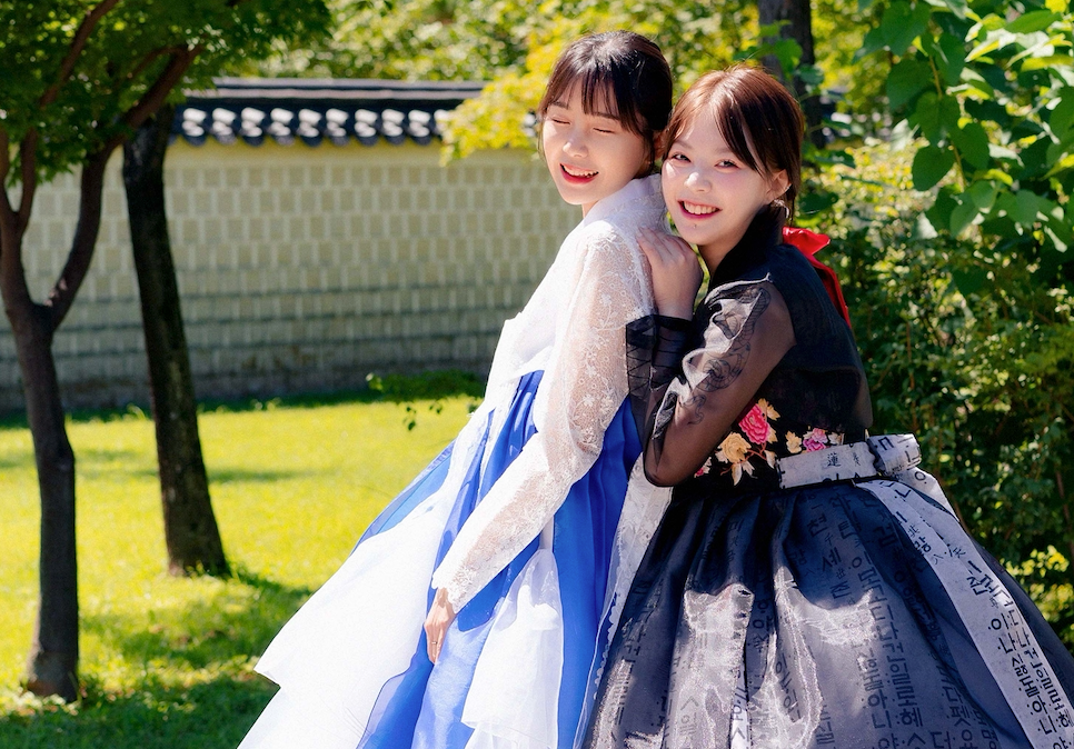 Two individuals standing closely, adorned in elegant hanboks. The hanboks feature rich colors and detailed patterns, exemplifying Korean traditional attire.