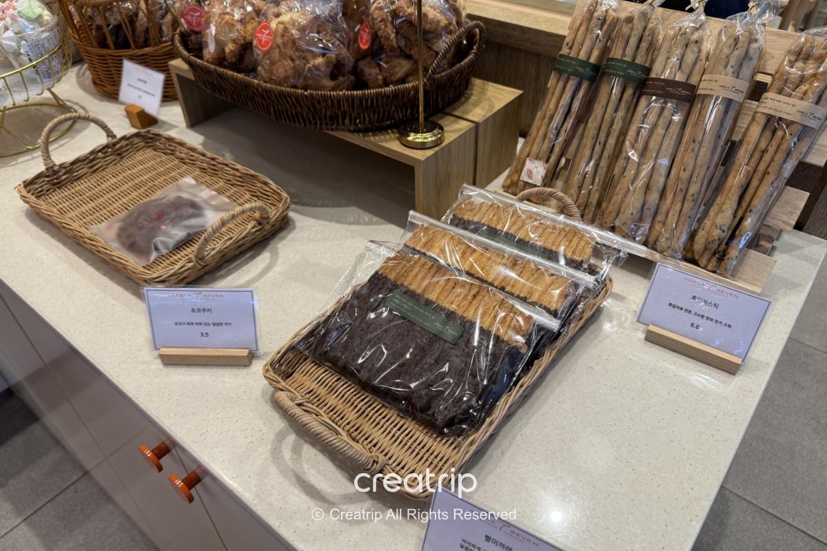 ADELA 7面包店的伴手礼展示：桌上篮子装有包装酥饼、长条饼干与面包，旁边标示价格，环境干净整齐，适合机场带走。