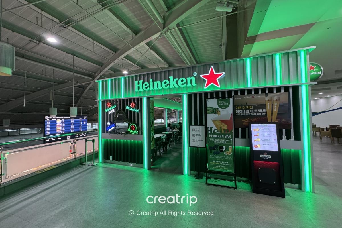 釜山金海机场4号登机门附近的Heineken Lounge Bar外观，绿色霓虹标志与酒吧入口、座位区及自助点餐机，适合登机前放松喝杯啤酒。