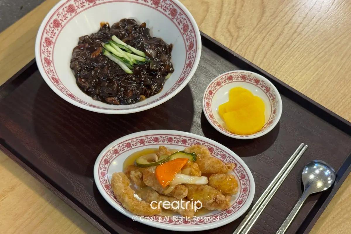 金海機場PLE美食街的炸醬麵與糖醋炸雞套餐擺在托盤上，附小碟醃蘿蔔與筷匙，呈現出發層可快速享用的韓式中華機場餐點