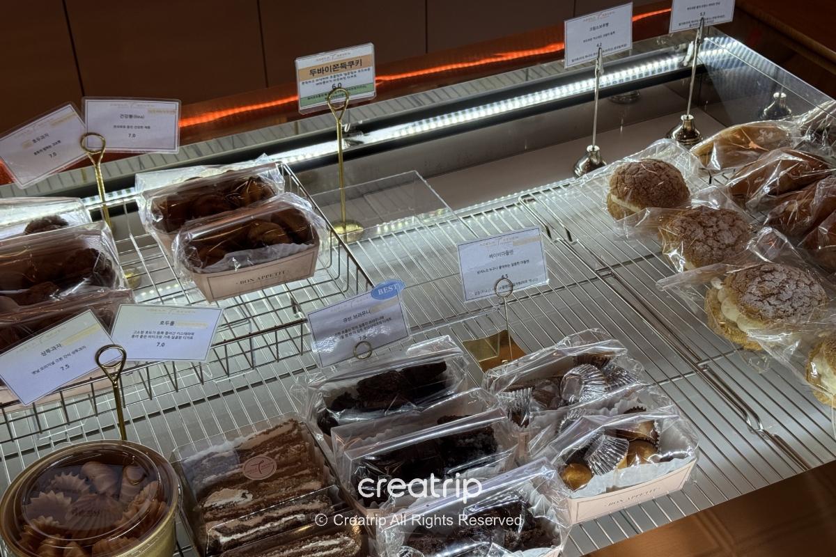 ADELA 7面包柜台展示多款包装面包与甜点，透明塑胶包装标示价格，适合刚抵达金海机场购买轻食或伴手礼