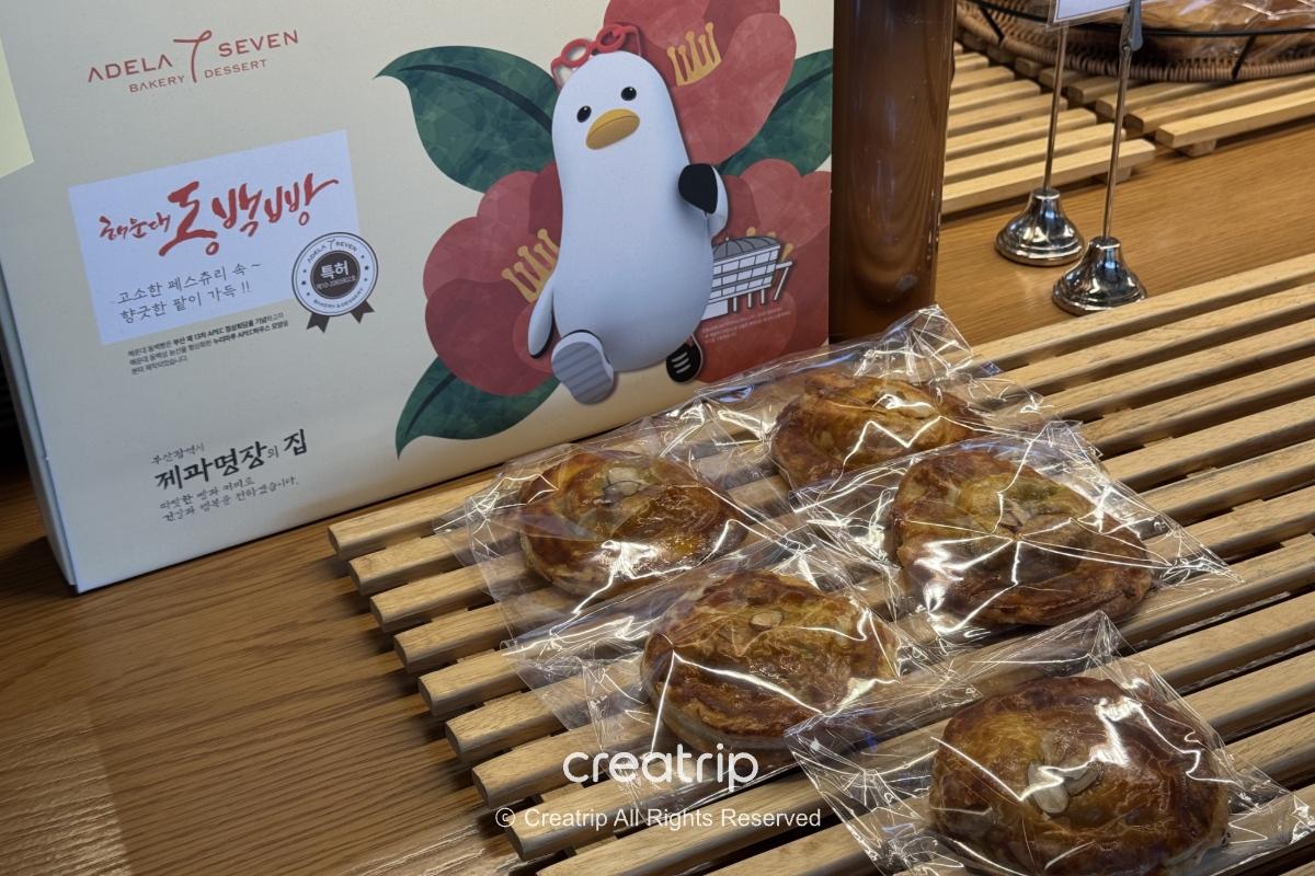 ADELA 7面包店展示包装精美的机张海带脆饼礼盒与六个单包装酥脆小点，放在木格栅展示台上，适合当机场伴手礼或轻食选择。