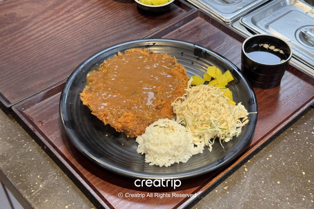 金海機場美食街的炸豬排套餐，盤中有淋上咖哩醬的酥脆豬排、白飯、沙拉與醃蘿蔔，旁邊有小碗湯，適合搭機前快速用餐的選擇。