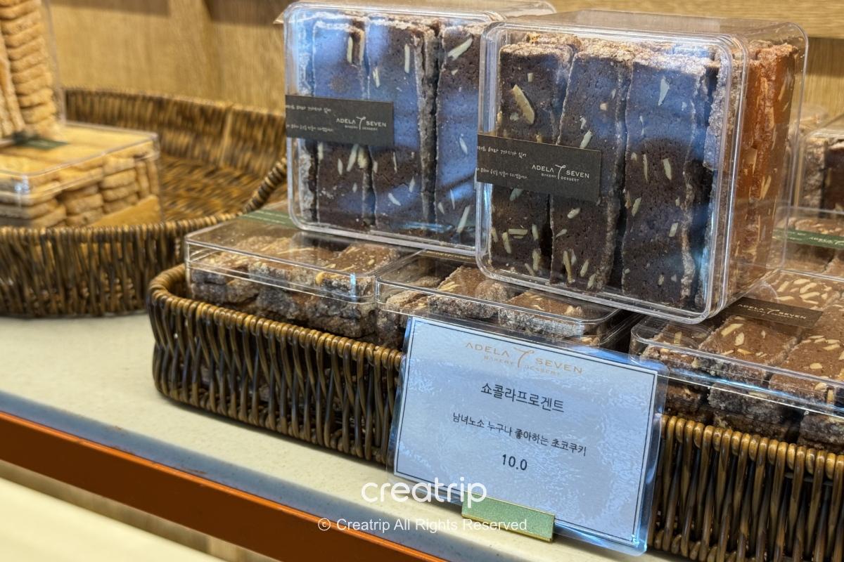ADELA 7面包店的包装巧克力饼干置于藤篮与透明塑盒中，店牌与价格标示清晰，适合作为釜山金海机场抵达层的伴手礼选择。