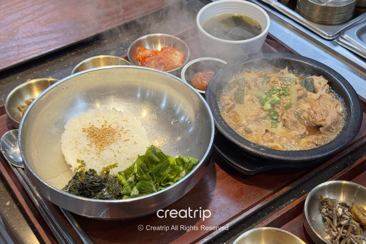 金海機場孝子牛骨湯的熱騰騰牛肉湯鍋與附白飯、海苔、生菜和小菜，鐵盤與石鍋擺在托盤上，適合抵達或出發前暖胃的一人份韓式套餐。