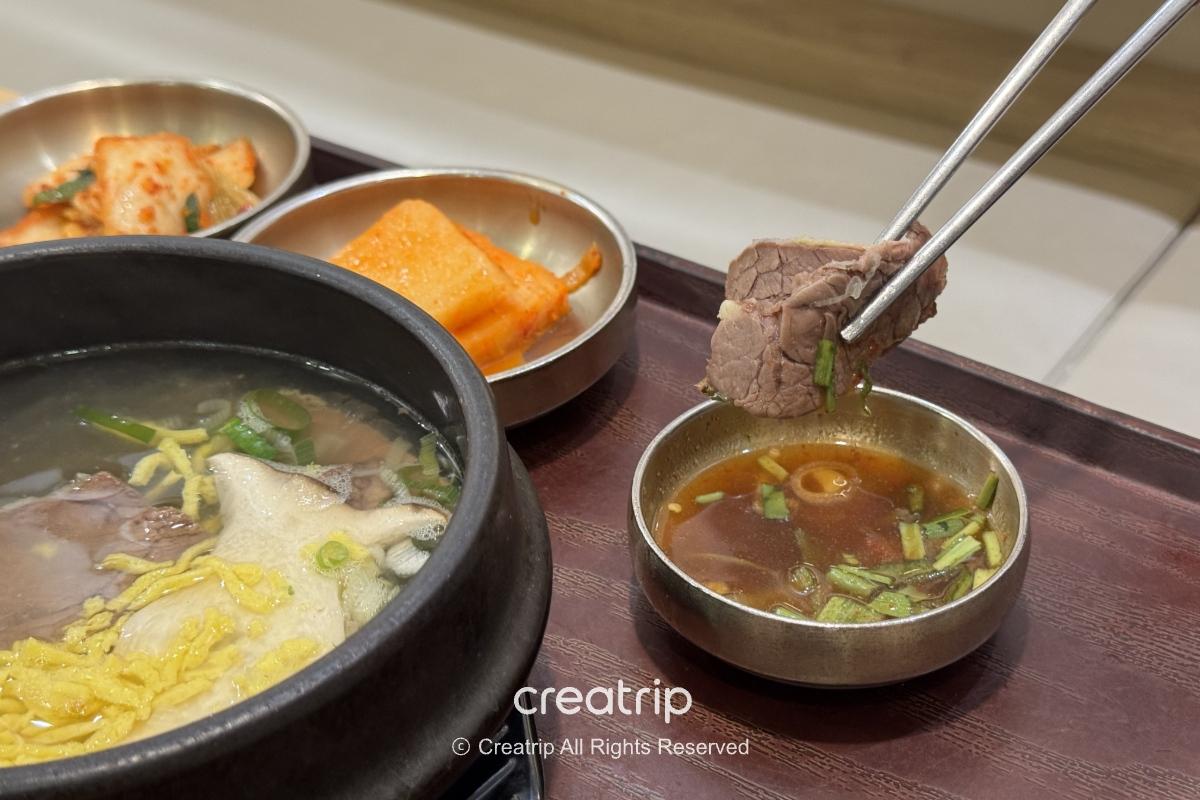 金海机场孝子牛骨汤的牛胸肉牛骨汤套餐特写：石锅热汤、切片牛肉、酱汁与小菜在托盘上，呈现暖胃的机场用餐选择。