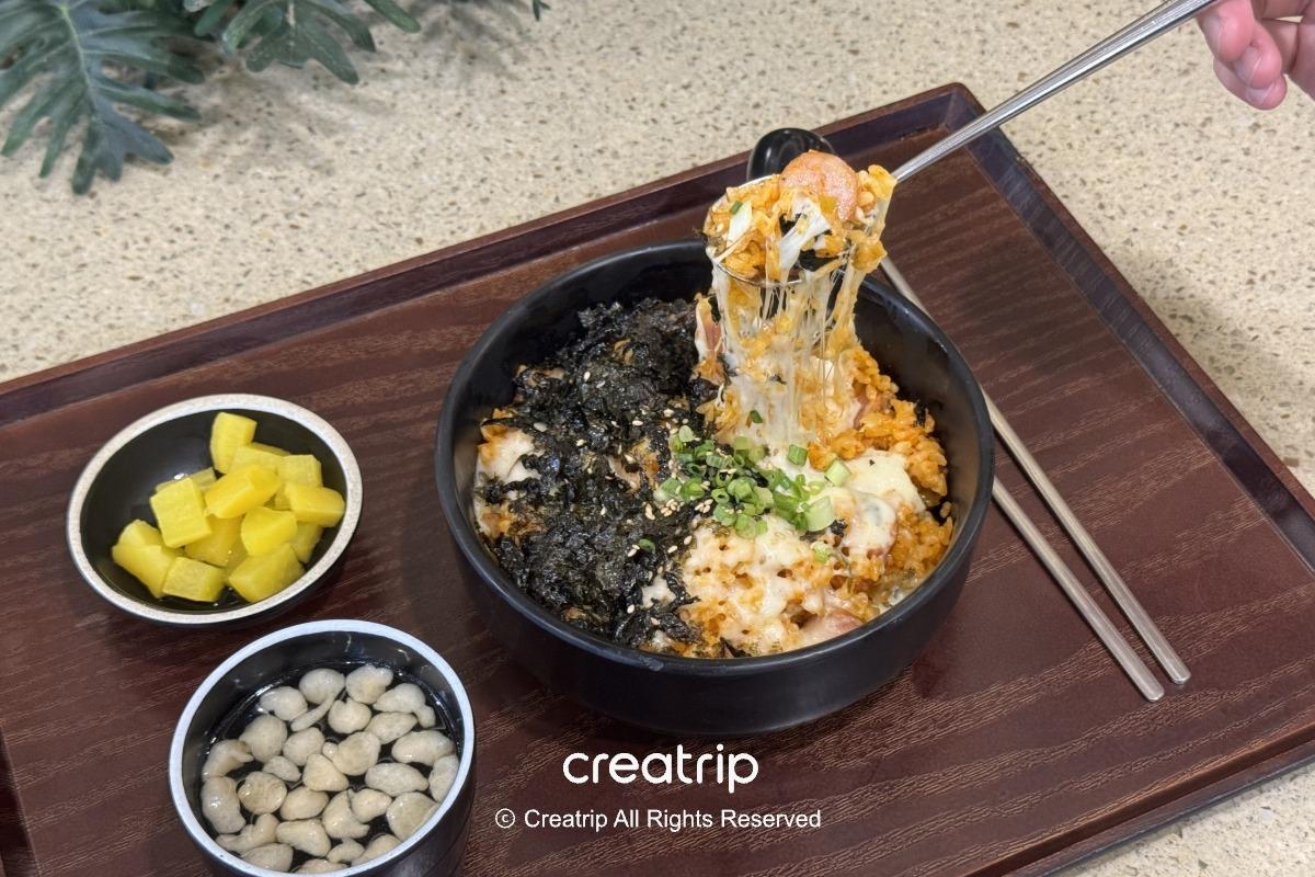 起司泡菜炒飯配海苔與蘿蔔小菜，筷子舉起牽絲飯糰呈現香濃拉絲感，適合在釜山樂天世界美食廣場快速填飽肚子
