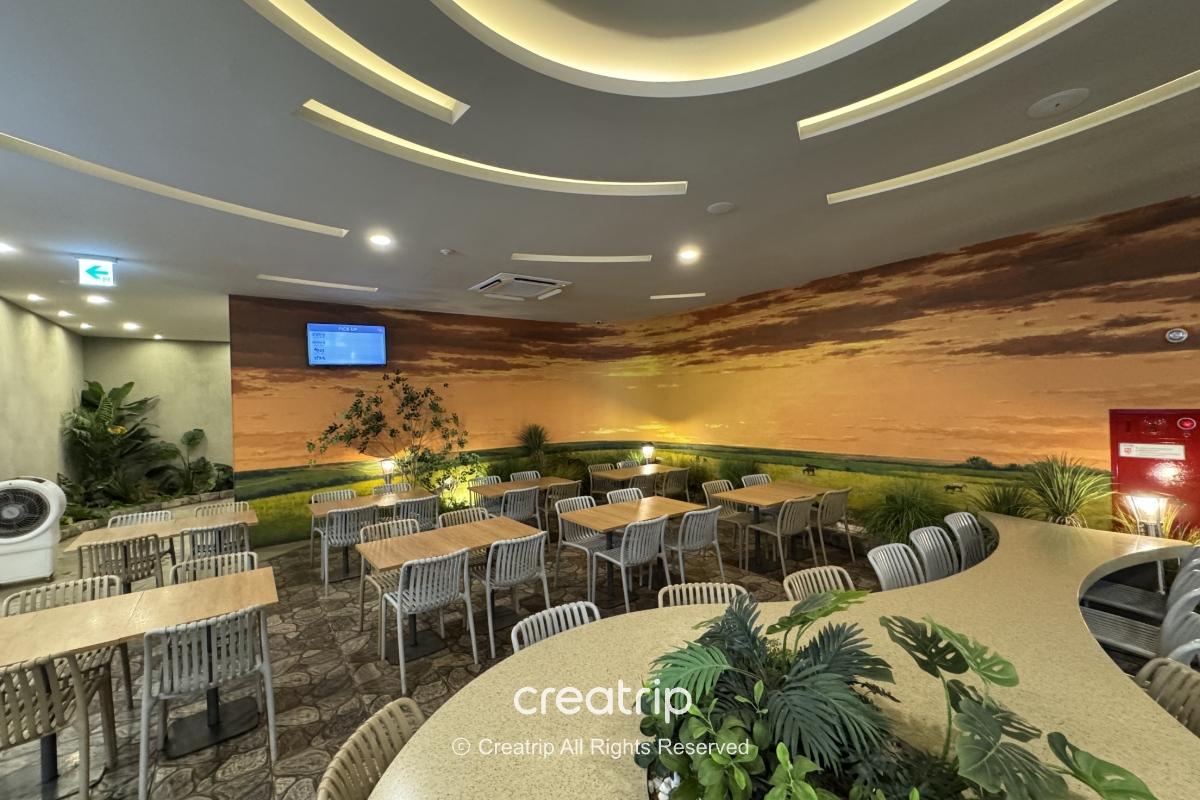 釜山樂天世界Joyful Food Plaza室內用餐區，寬敞座位、冷氣舒適、牆面草原夕陽壁畫，適合家庭與團體休息用餐