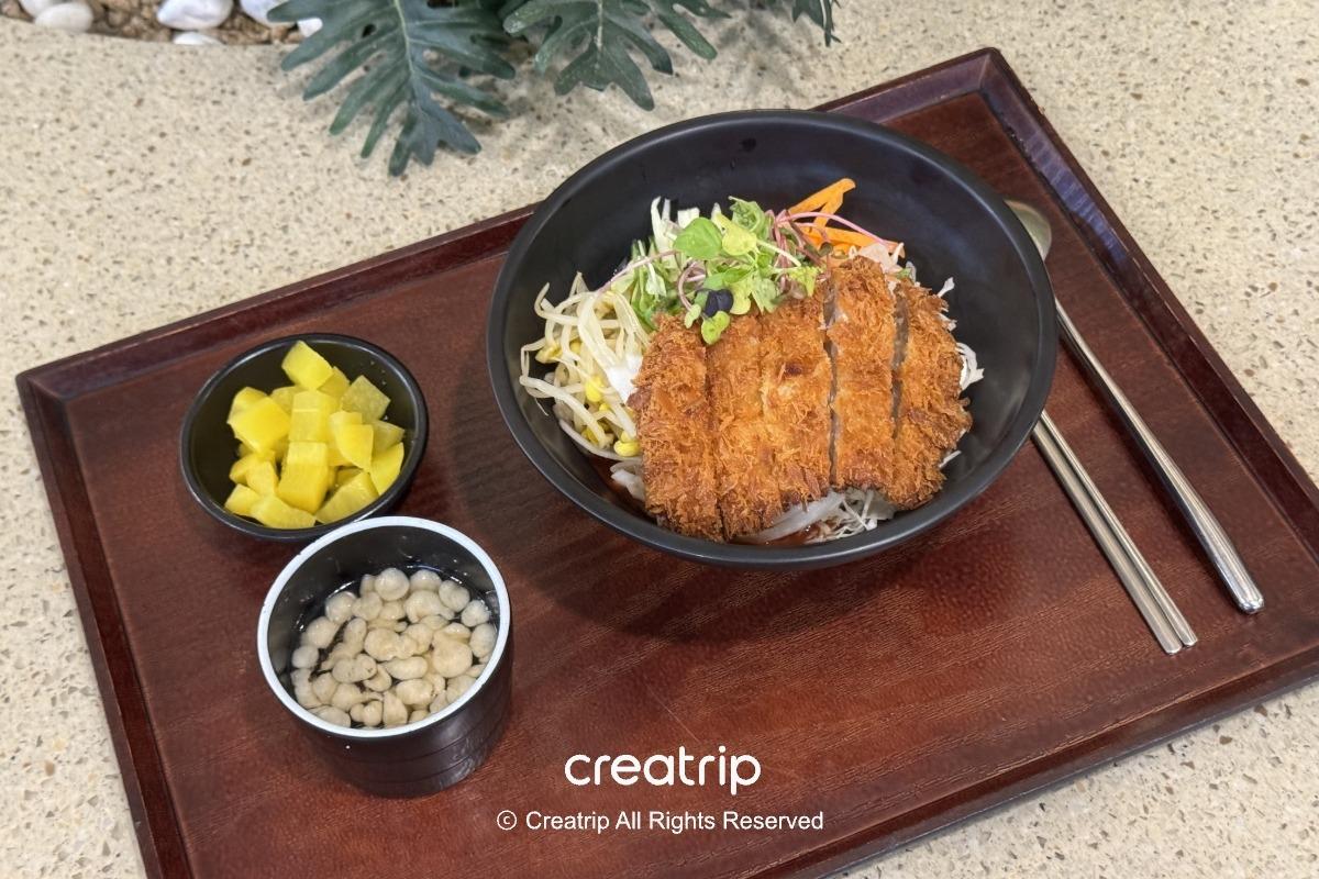 釜山樂天世界Joyful Food Plaza的炸豬排蓋飯套餐，黑碗裝炸豬排搭配生菜、豆芽與醬汁，附小碟醃黃蘿蔔與湯品，木托盤擺盤整潔適合家庭用餐