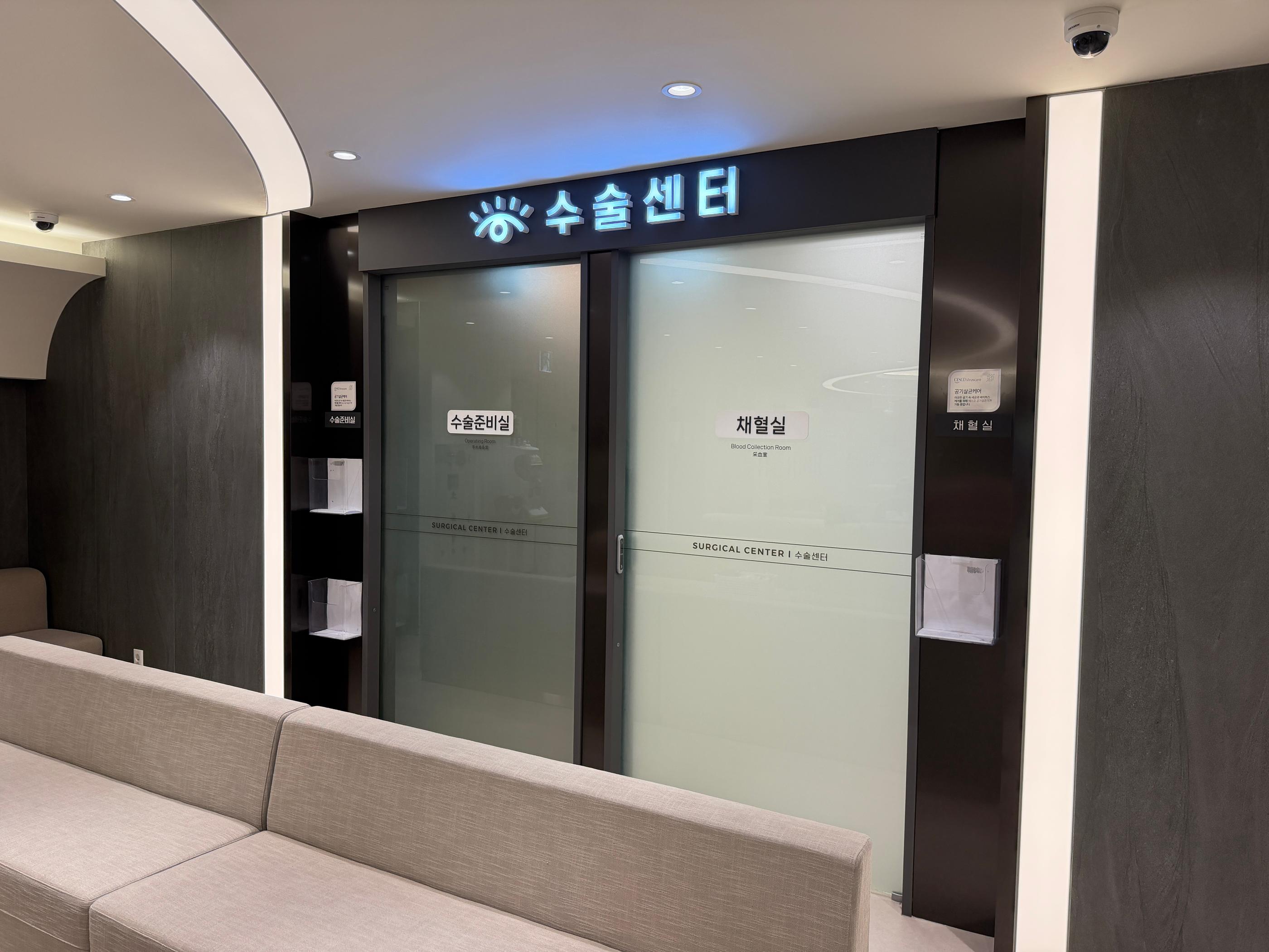 江南明亮聖母眼科手術中心門口候診區：灰白色沙發、玻璃手術室門與韓文標示，展現整潔舒適的術前等候動線與醫療環境。