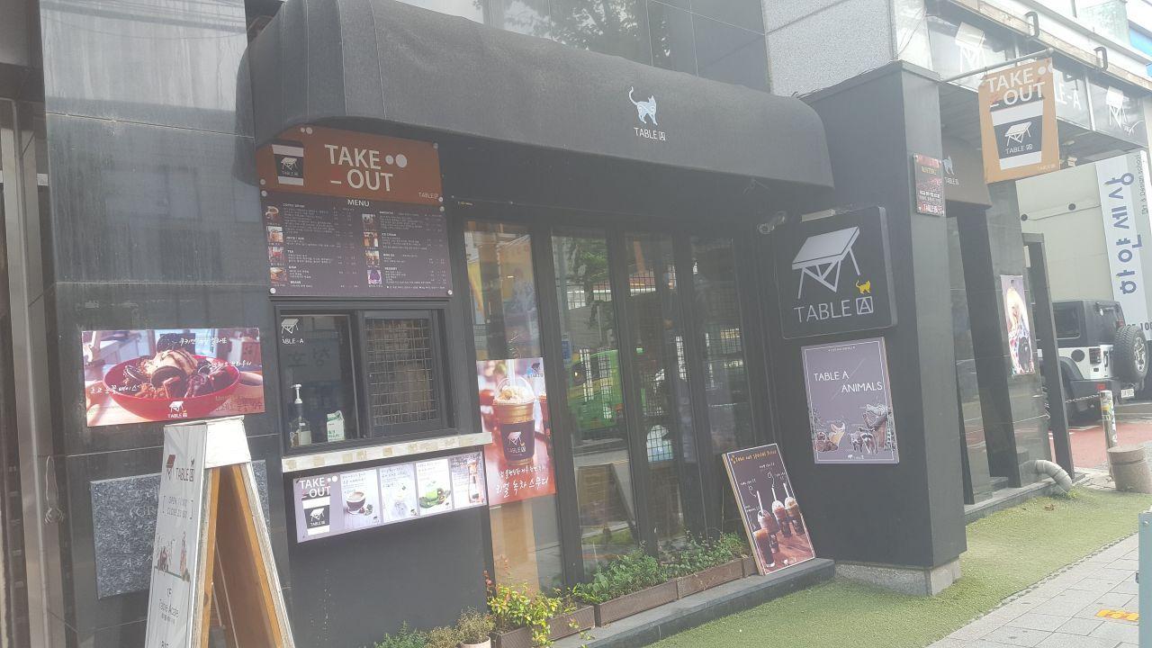 Exterior of Table A, a cat café located near Hongik University Station in South Korea, showcasing a dark storefront with various café posters and a take-out menu.