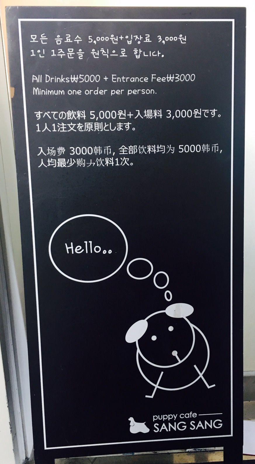 Entrance sign of Puppy Cafe Sang Sang, highlighting entry fees and drink costs in multiple languages for international visitors.