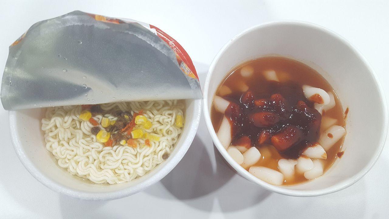 Opened cup noodles and spicy rice cake package with sauce and hot water added, displaying the initial preparation steps for Mark meal.