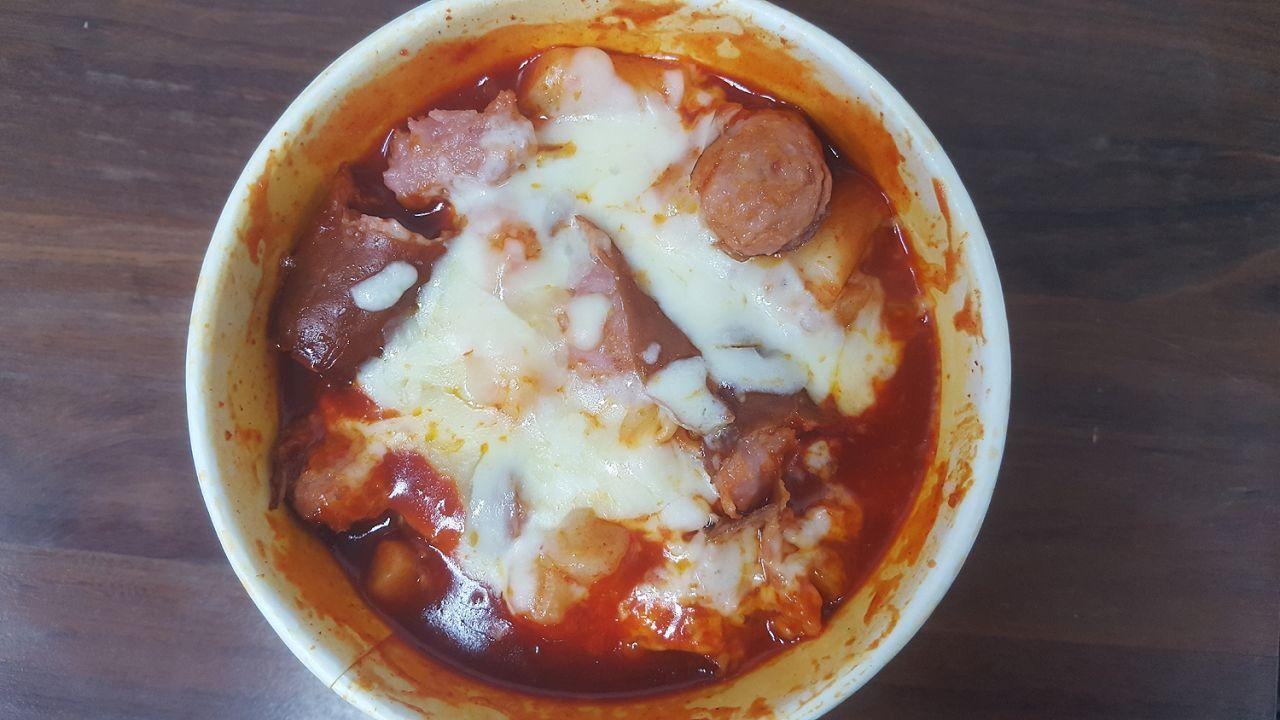 Melted cheese and cooked sausage over rice cakes and noodles in a bowl, showcasing the hearty and savory appearance of the Mark meal.