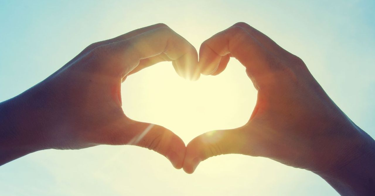 Hands forming a heart shape against the sunlight, symbolizing love and affection.