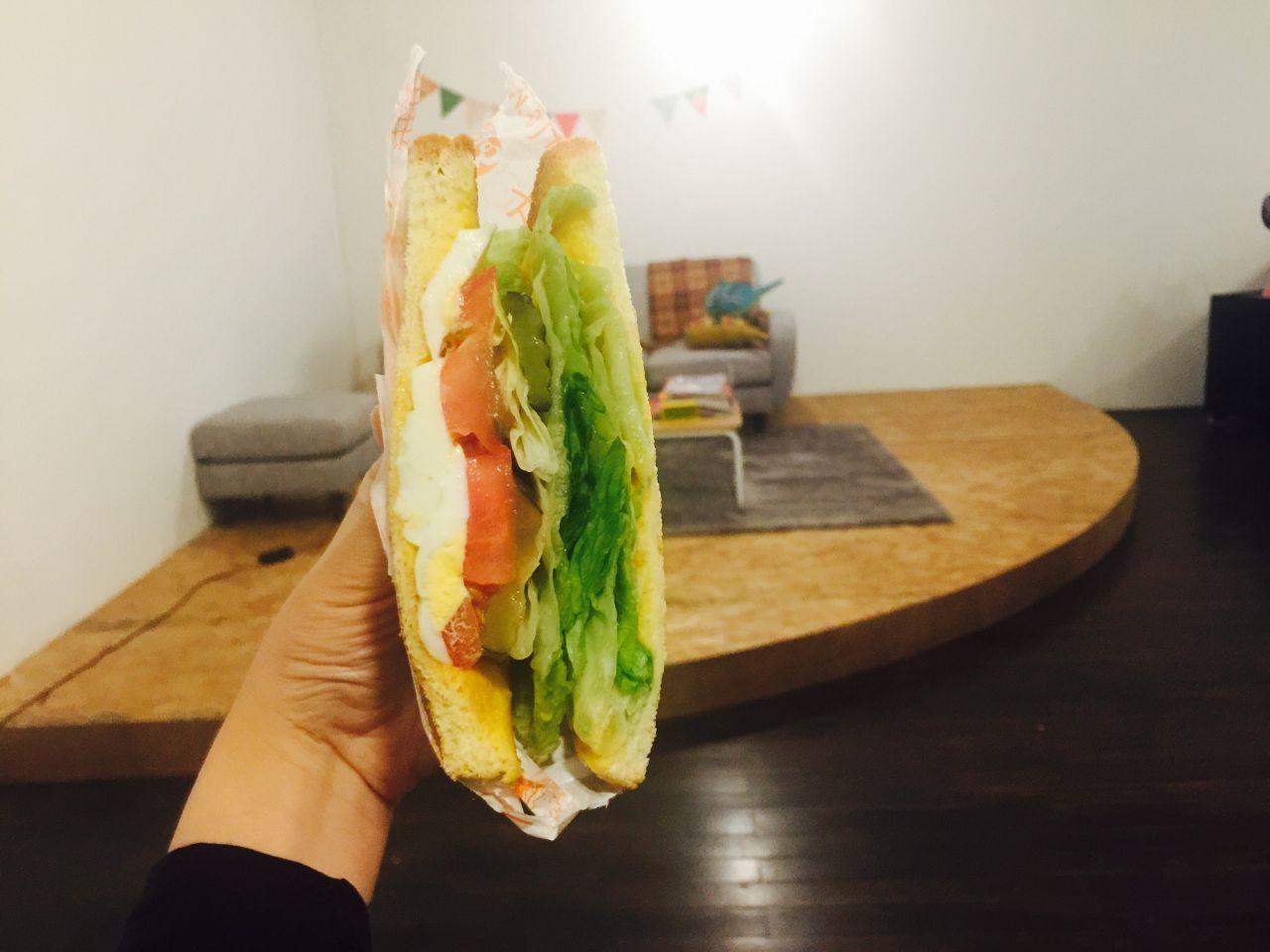 清新的三文治舉在空中，瞬間捕捉到新鮮蔬菜與吐司的完美結合，是甜蜜cafe最受歡迎的早餐搭配之一。