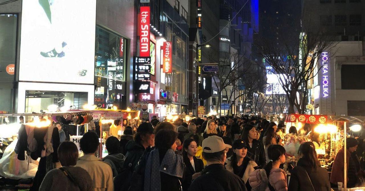 Vibrant and crowded shopping street in Myeongdong featuring various shops and attractions at night.
