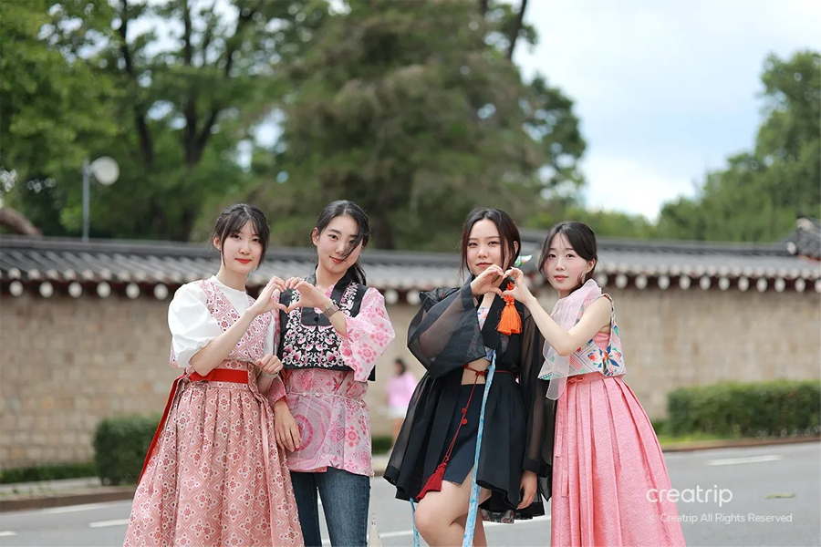 Four individuals wearing vibrant and stylish hanbok outfits, posing together in front of a historic backdrop, showcasing the beauty of Korean traditional clothing.