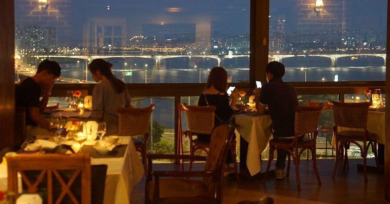 韓國城市夜景下的浪漫餐廳，數對情侶在用餐，營造出約會氛圍。