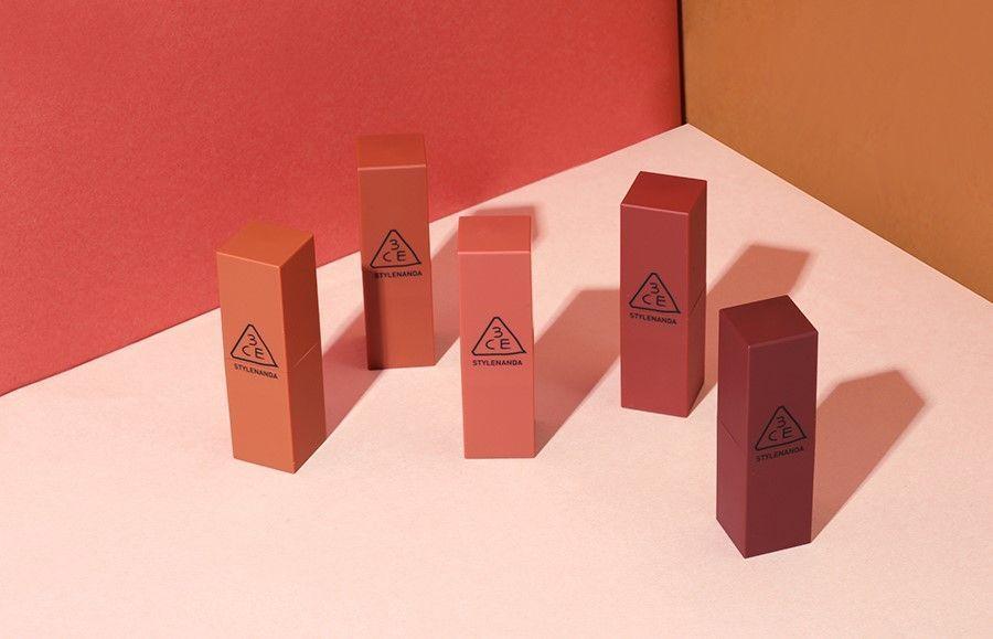 Collection of 3CE lipsticks showcasing different fall-themed shades against a pink and orange backdrop.