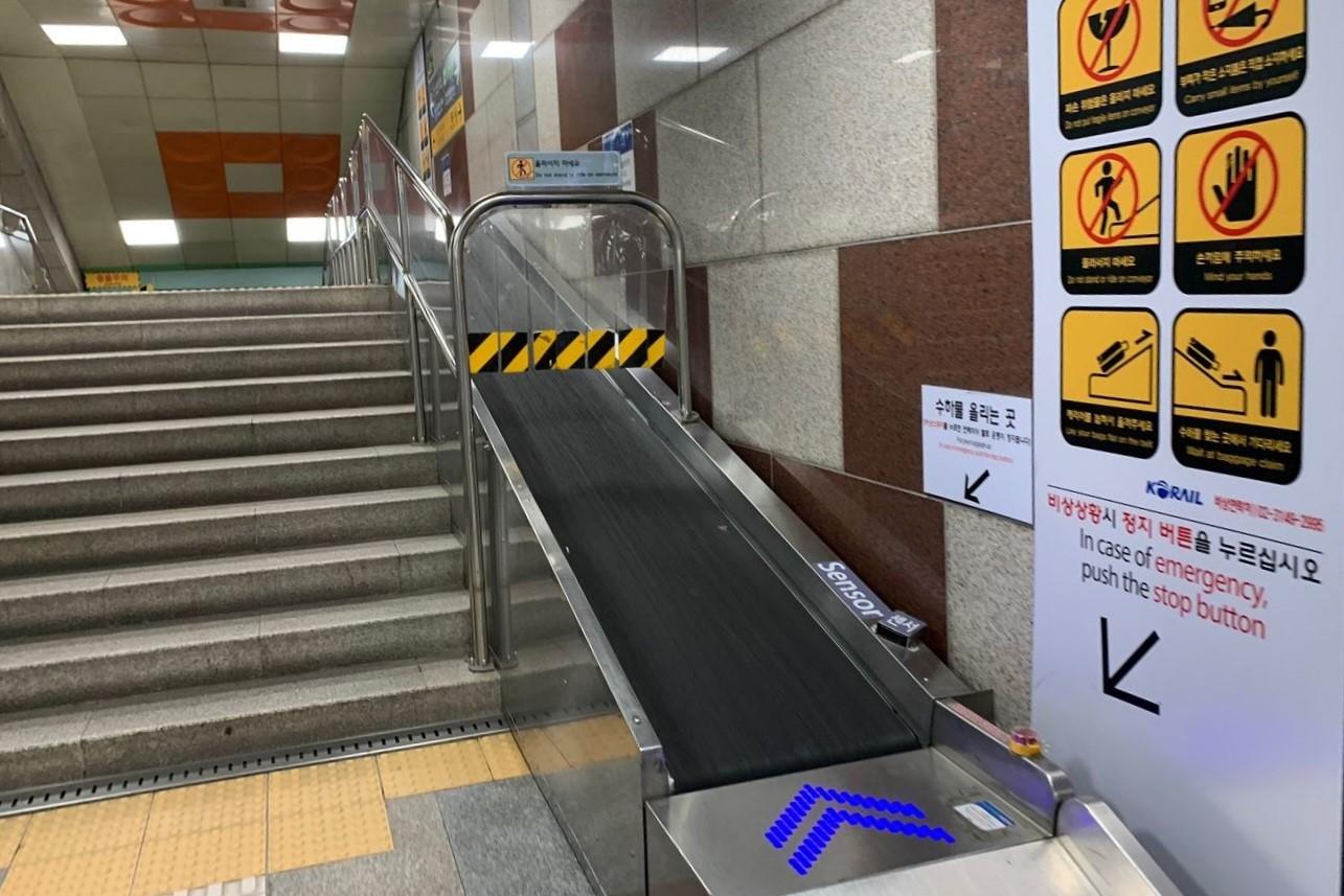 地下鉄駅の階段と荷物運搬用ベルトコンベア、韓国の公共交通の特徴的な設備を表示。