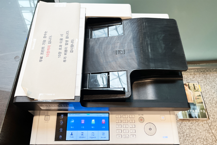 在仁川机场的商务中心打印机，为长途旅客提供便利。图片中展示了一台多功能打印机，适用于打印、扫描、复印和USB传输功能，顶部有张贴的使用指示和注意事项。