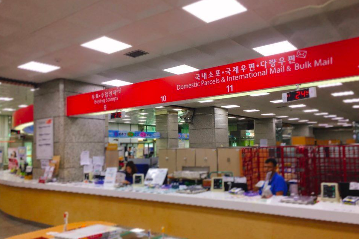 Interior view of a Korea Post office featuring the Domestic Parcels & International Mail & Bulk Mail counter, indicating areas for postal services for both domestic and international mail.