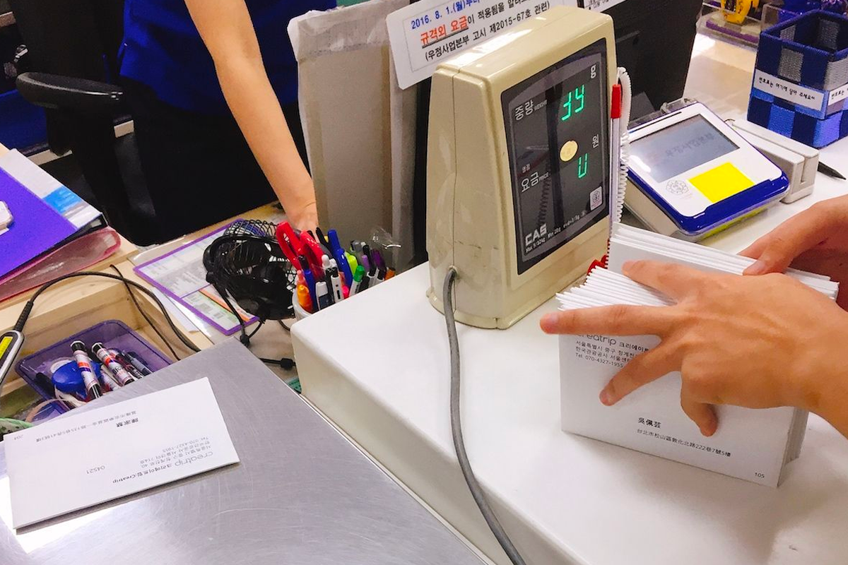 Digital scale and postal forms at Korea Post used for weighing packages and calculating postage costs, part of the mailing process at postal counters.