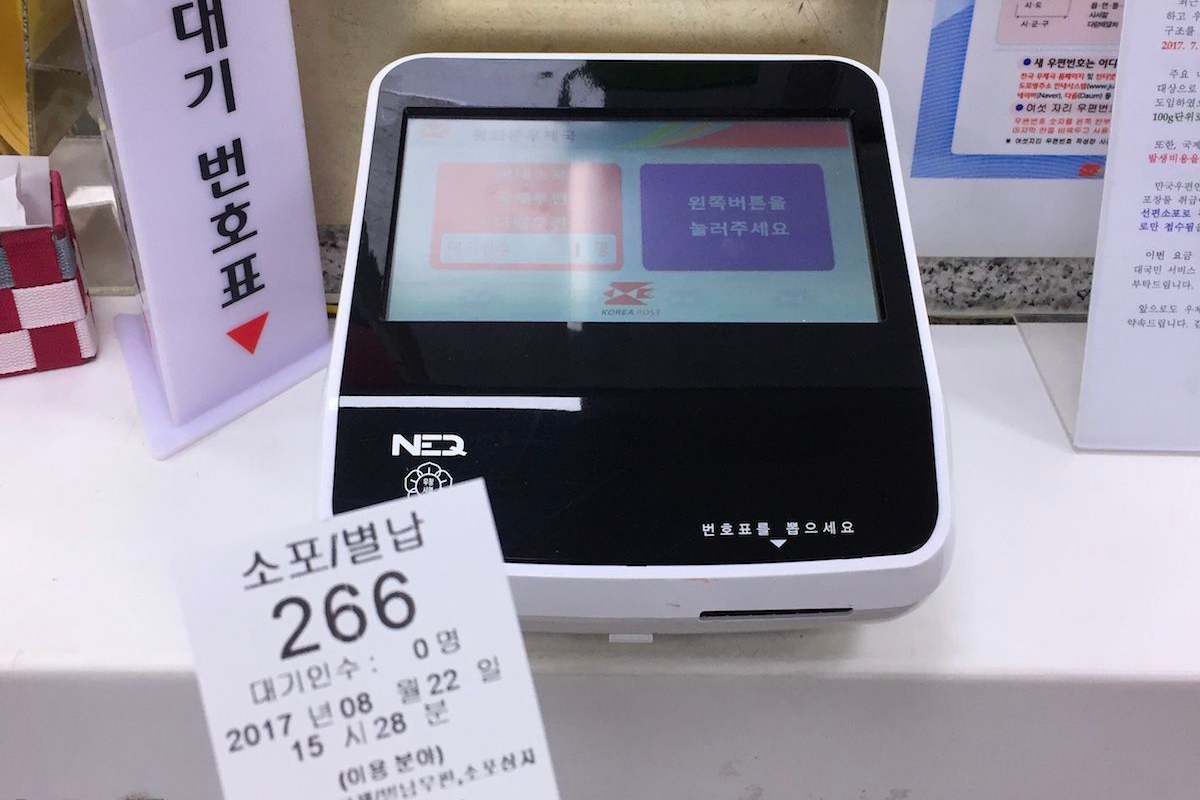 Ticket machine at a Korea Post office for taking numbers to wait for service, indicating an organized customer service process.