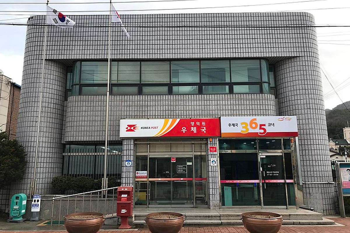Exterior view of a Korea Post building with flags and Korea Post signage, showcasing the official postal service location in Korea.