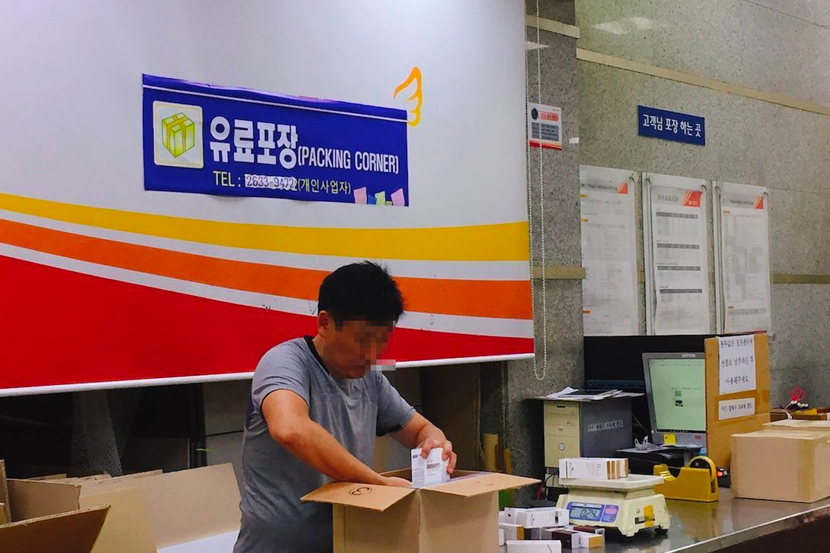 A packing corner in a Korea Post office with a person assembling boxes, demonstrating the preparation of parcels for shipping.