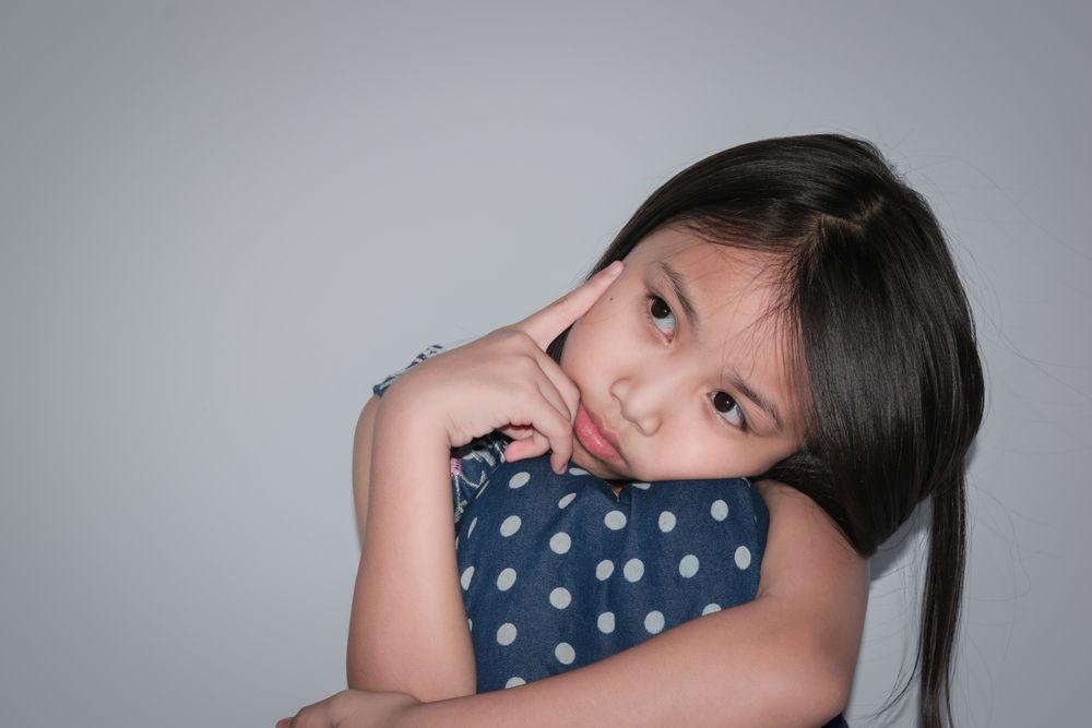 Young girl with long dark hair posing against a plain background.