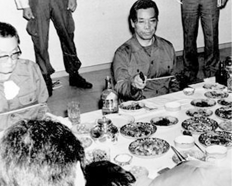 一羣人在餐桌前用餐, 前方擺放著豐盛的韓國料理，中間舉著筷子的人似乎在發表意見。