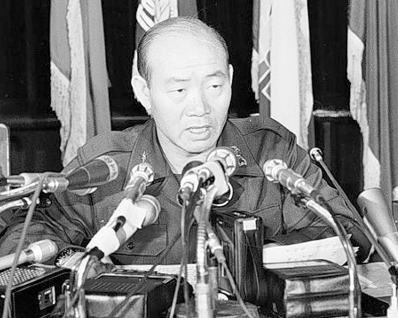 1980年的光州，警察防線前站立著大量示威羣眾，背景是韓國的大學校園入口。