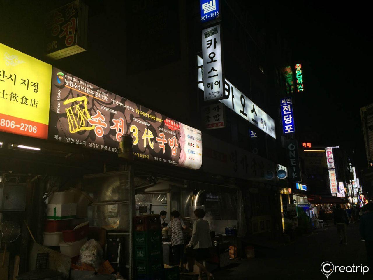 Night view of Songjeong 3 Generations Rice Soup restaurant in Busan, highlighting its long-standing reputation for Busan-style pork rice soup.