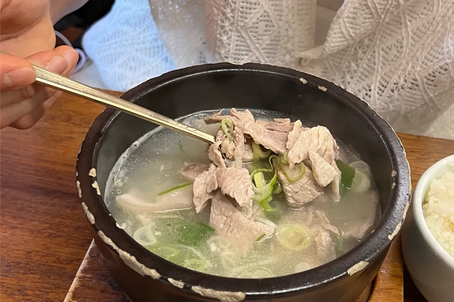 这张图片中的食物是韩国传统的猪肉汤饭，配菜繁多，搭配鲜美的汤汁，是釜山旅行时不得不尝的传统美食。