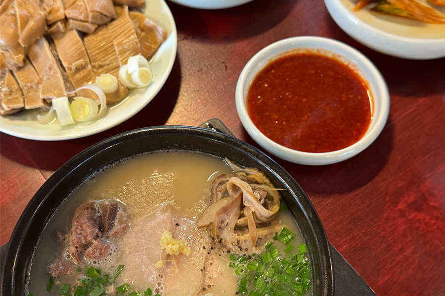 这张图片展示了在釜山旅行期间，你可以在许多餐馆品尝到的地道韩国猪肉汤饭。这道美食以浓郁的汤底和细嫩的猪肉闻名。