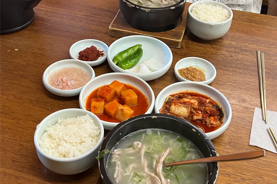 显示了韩国釜山的餐桌上，色彩鲜艳的配菜搭配香浓的猪肉汤饭，是典型的韩式用餐场景。