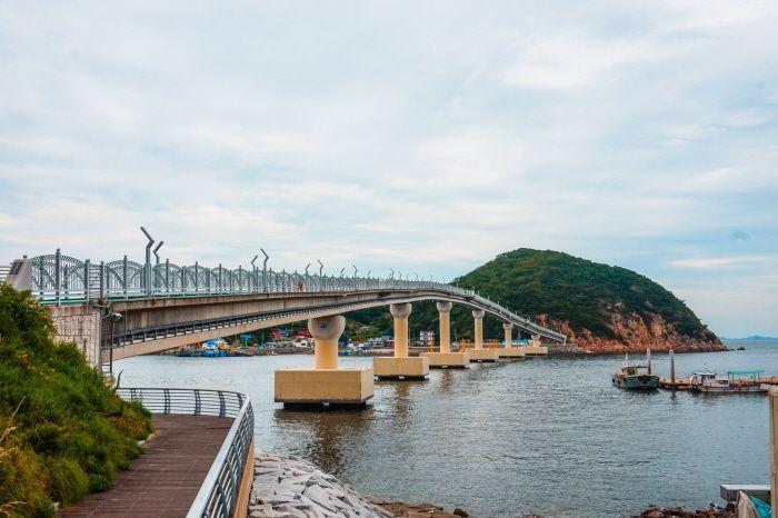 A picturesque bridge connecting to Muido Island, with serene water beneath and lush green hills in the distance.