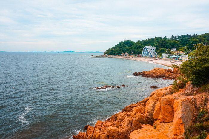 Rugged rocky coastline of Muido Island, with waves gently lapping against the shore under a tranquil sky.